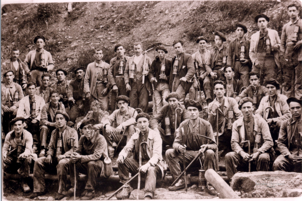 foto en blanco y negro en la que se ve un grupo de mineros posando a la entrada de la boca de una mina. 