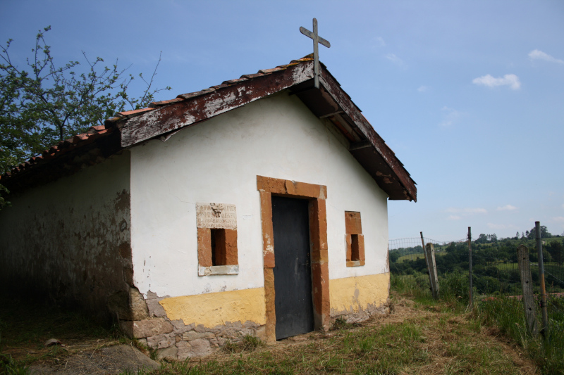 foto frontal de la Capilla de San Lorenzo en el pueblo de Loriana.  Es una pequeña capilla blanca con dos pequeñas ventanas hechas de caliza roja que flanquean la puerta central. En una de las ventanas hay tallada una lápida con  una inscripción sobre la iglesia.
